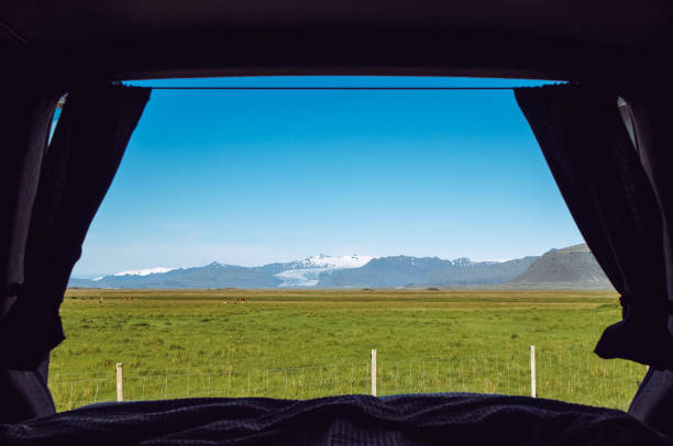 istock Looking out the camper minivan back from built in bed. Traveling Iceland with van. View over mountains, pasture and glacier, blue sky, sunny day. 1411057818