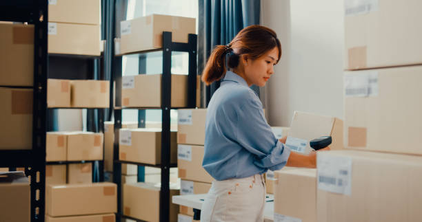 istock Asian businesswoman standing front of shelf use barcode machine scan customer data in box on desk register online detail information for express delivery at warehouse. 1411058525