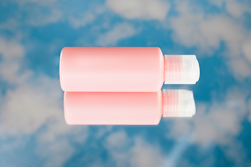 Moisturizing cream bottle on mirror with cloudy sky reflection. Product mockup.