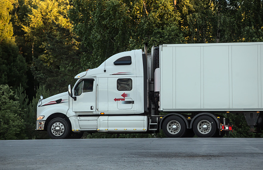 white truck moves along a suburban highway along the forest.