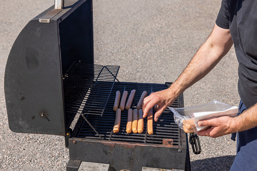 Close up view of man's hands grilling sausages on grill. Sweden.