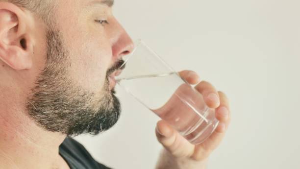 istock A young man drinks water from a glass 1411067677