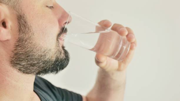 istock A young man drinks water from a glass 1411067726