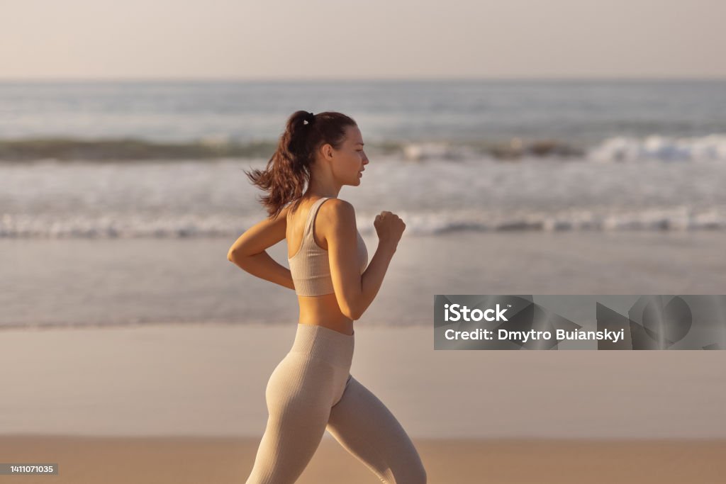 Female Runner Jogging During Outdoor Workout on the Beach Running woman. Female runner jogging during outdoor workout on beach. Beautiful fit fitness model outdoors. High quality photo Running Stock Photo