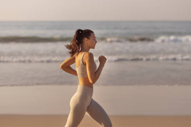 female runner jogging during outdoor workout on the beach - running women jogging profile imagens e fotografias de stock