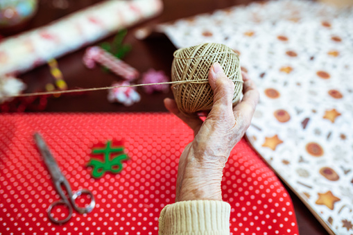 A closeup of an old woman's hand holding a ball of rope while wrapping Christmas presents