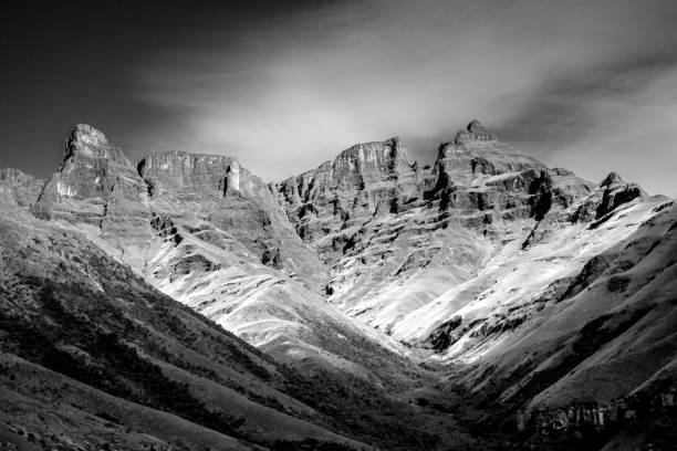 Black and White view of the tall craggy cliffs in the Injisuti region of the Drakensberg Mountains on a clear sunny day. These iconic cliffs and peaks of the Drakensberg Mountains formed due to the combination of the Jurassic period large flood basalt during the break-up of the Gondwana Supercontinent and erosion from the later uplift of the African Continent. The Drakensberg Park were declared a Unesco World Heritage site in 2000 to protect the natural habitats, but also due to its cultural significant since it has the largest concentration of rock paintings in Sub Sahara Africa.