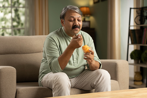 Mature man having ice cream sitting on sofa