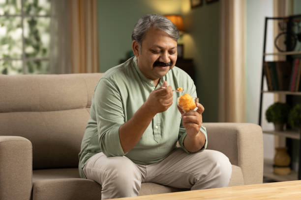 istock Mature man having ice cream sitting on sofa stock photo 1411072437