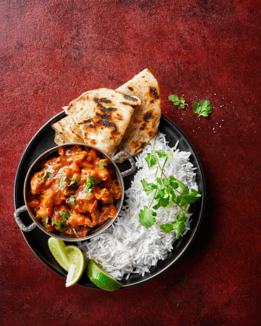 Chicken tikka masala spicy curry meat food Butter chicken, rice and naan bread on red vine dark background. Traditional Indian dish, top view, close up, copy space.