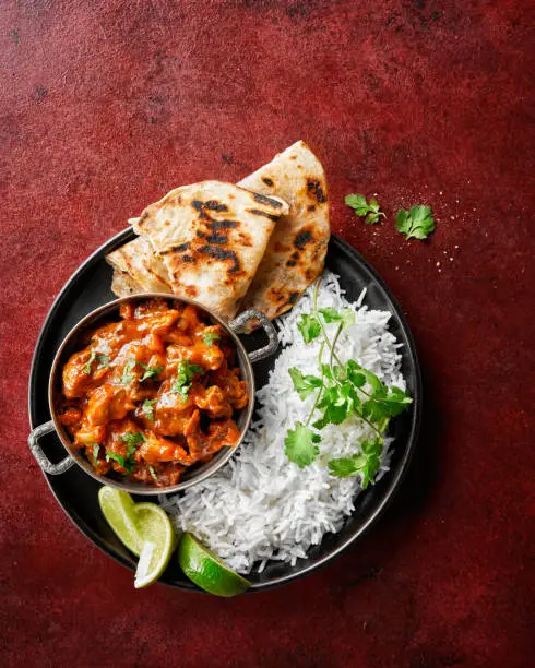 Photo of Chicken tikka masala spicy curry meat food Butter chicken, rice and naan bread on red vine dark background. Traditional Indian dish.