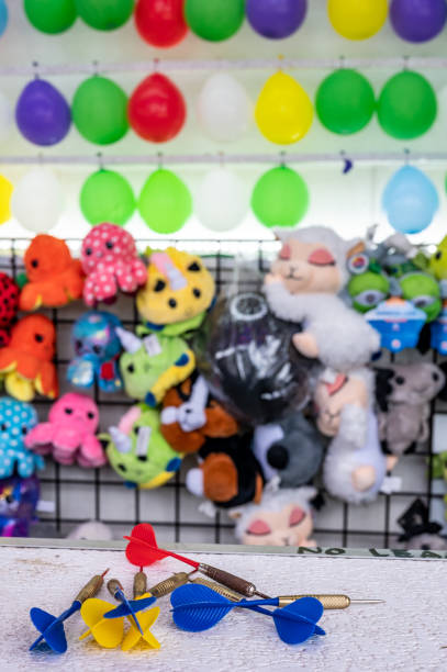 istock selective focus on darts sitting on a ledge with a wall of balloon targets and prizes that a player can win at a fair. 1411076335