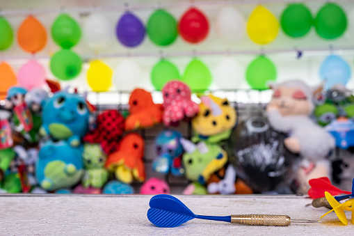 selective focus on darts sitting on a ledge with a wall of balloon targets and prizes that a player can win at a fair. High quality photo
