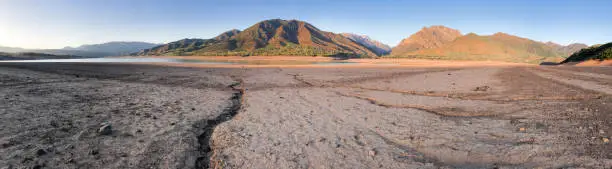 Photo of Panorama beautiful landscape with setting sun: mountains, lake and cracked earth - dried-up riverbend. Copy space
