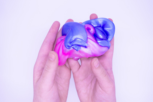 Two-color blue and pink slime in someone hands on a white background. The mucus is crushed, stretched, torn and squeezed.
