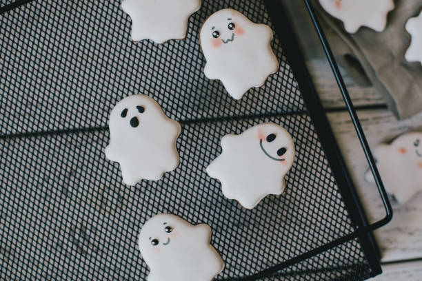 istock Funny scary Halloween ghost cookies with white icing on black tray. 1411082615