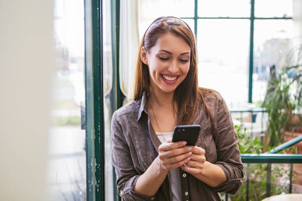istock Smiling beautiful young woman at a windowsill and texting 1411088894