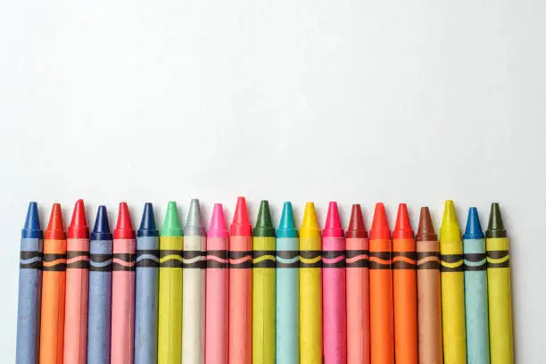 Photo of Multicolored crayons lined up on white background.