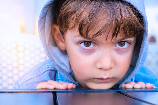 Sad, pensive little boy wearing a hood looking at the camera