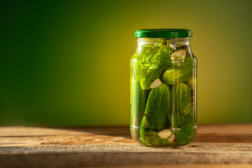 Pickled cucumbers in glass jars on green background.