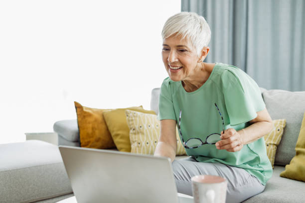 istock Senior woman using laptop while relaxing at home 1411095975