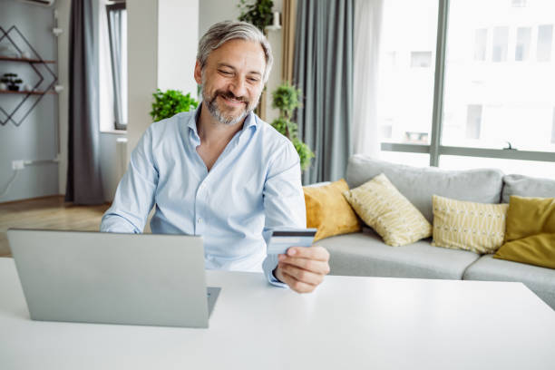 istock Mature man holding a credit card and using a laptop 1411097681