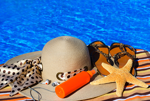 Starfish, headphones, sun spray, women's hat and flip flops on the background of the pool concept of relaxation. Summer family vacation concept