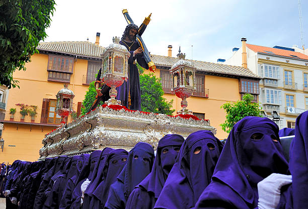 Costaleros bearing a Tronos during Semana Santa in Malaga, Spain A group of hooded bearers (called Costaleros) carrying a religious float (known as a Tronos) in the processions held in Malaga to celebrate Semana Santa (Easter Holy Week). Up to 250 costaleros may be required to carry the largest tronos, which can weigh several tonnes, and the processions can last many hours. holy week photos stock pictures, royalty-free photos & images
