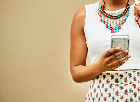 Cropped shot of a stylish woman texting on her cell phone against brown background
