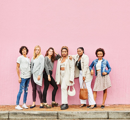 Portrait of a group of stylish man and women standing in front of a pink wall outside