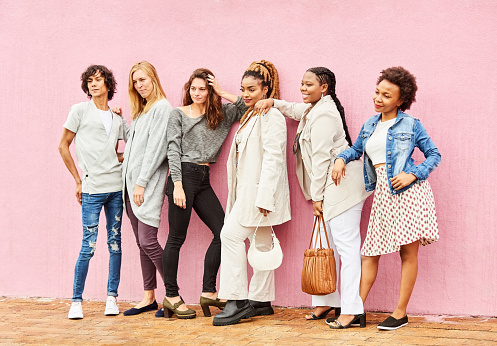 Portrait of a multiracial group of people wearing stylish outfits standing together in front of a pink wall outside