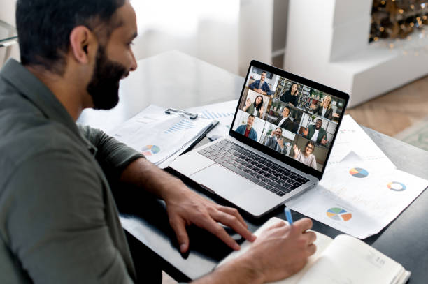 istock Business briefing. Indian guy looking at laptop screen, talking on video call with multinational business group, holds conference, virtual meeting, brainstorming with colleagues online, takes notes 1411110336