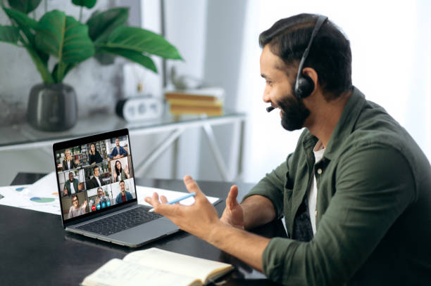 istock Successful busy mixed race successful man, sitting at work desk in modern office, using laptop talking to multiracial business team via video conference. Virtual online meeting, remote negotiations 1411110344