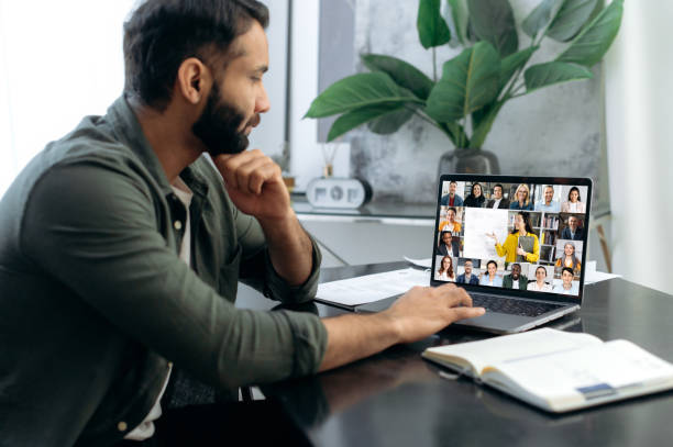 istock E-learning, Online education, webinar. Focused successful smart mixed race man listening to an online lecture, taking notes in notebook, on a laptop screen, a teacher and a group of multiracial people 1411110365