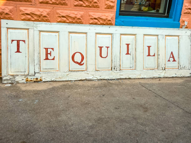 Rustic Tequila Sign The word Tequila playfully spelled out on individual cabinet doors. Red lettering against white rustic cabinet doors. Paint is chipped and peeling from outdoor wear. Sign rests on the ground and is standing up against adobe style orange bricks. adobe material stock pictures, royalty-free photos & images