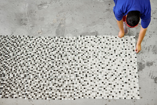 High angle view of a worker placing sheets of mosaic tiles on the floor of a manufacturing warehouse for inspection