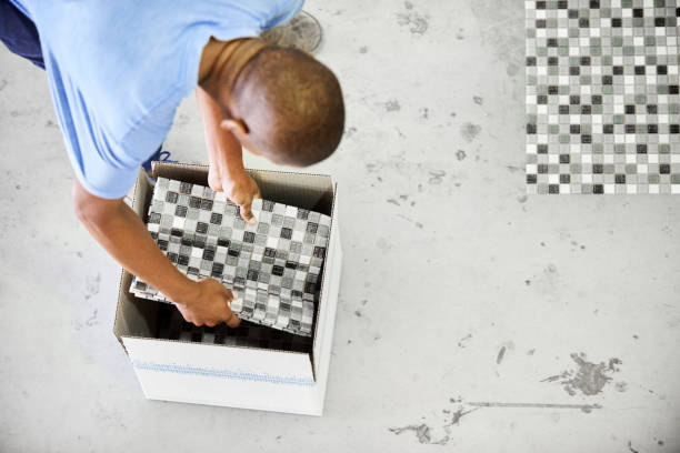 Worker picking up sheets of tiles from a factory floor and placing them in to a box for shipping