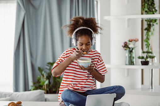 African girl is at home, she is using a digital tablet and eating breakfast