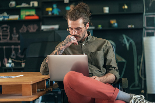 Young modern businessman using laptop at the office. Man with tattoos working in modern creative office.