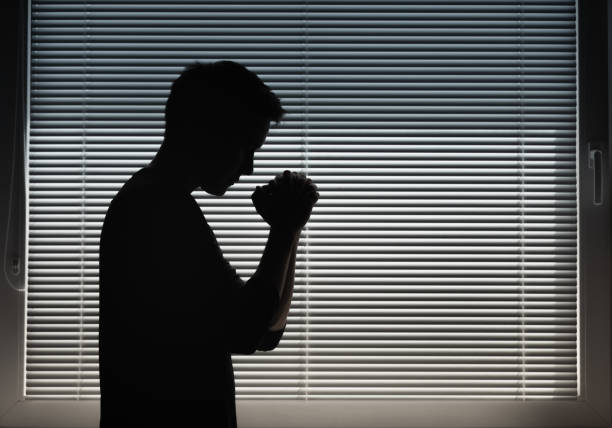 istock Man saying a prayer indoors next to window. 1411116046