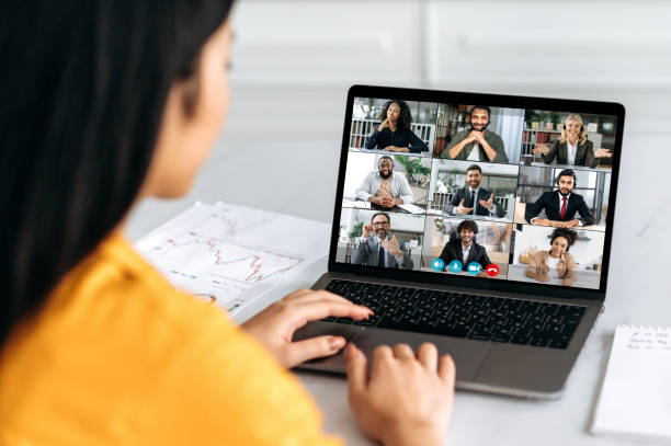 Online video conference, group brainstorm. Over shoulder view of girl on a laptop screen with group of multiracial business people talking on a video call, discussing business project, business plan stock photo