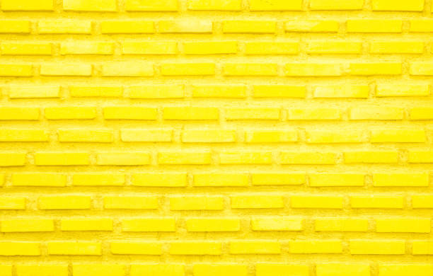 istock Brick wall painted with yellow paint pastel bright tone texture background. Brickwork and stonework flooring interior with rock old pattern clean grid concrete uneven bricks design backdrop. 1411123958
