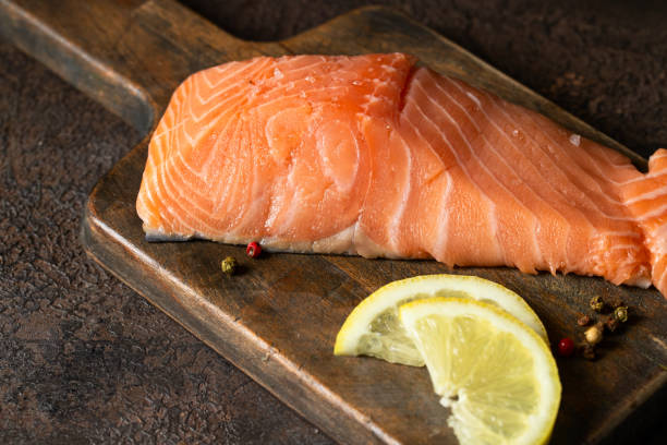 istock Uncooked salmon fish slice with lemon on wooden try ready for cooking. Copy space 1411124094
