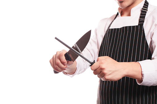 unrecognizable chef sharpens his knife on white background and there is free space at left side