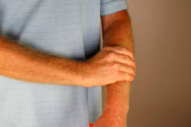 Front view close-up of a mature caucasian male massaging his left forearm with his right hand. Left caucasian forearm of a man being self-massaged by his right hand up close while wearing a blue shirt