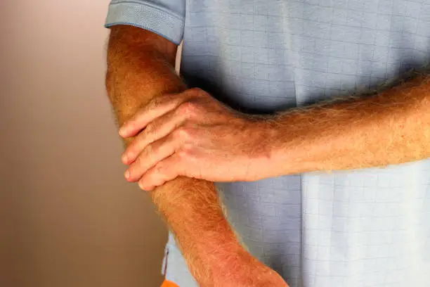 Adult caucasian man massaging his right forearm with his hand and fingers close-up. Adult man with a blue shirt on massaging his right forearm with his left hand and fingers to relieve muscle tension.