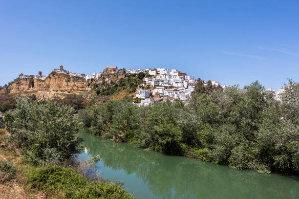 White houses in Arcos de la Frontera along  Guadalete river, Andalusia, Spain, Arcos de la Frontera is a town and municipality in the Sierra de Cádiz Comarca, province of Cádiz, in Andalusia, Spain. It is located on the northern, western and southern banks of the Guadalete river, which flows around three sides of the city.  The town commands a fine vista atop a sandstone ridge, from which the peak of San Cristóbal and the Guadalete Valley can be seen. The town gained its name by being the frontier of Spain's 13th-century battle with the Moors. jerez de la frontera stock pictures, royalty-free photos & images