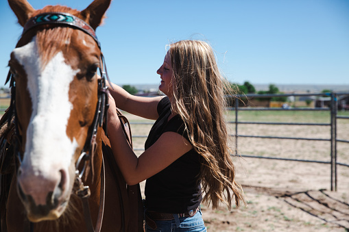 Happy smiling young teenage girls standing outdoors together with their brown horse after a horseback ride. Smiling happy together side by side towards the camera. Real People Horseback Riding Lifestyle Portrait.