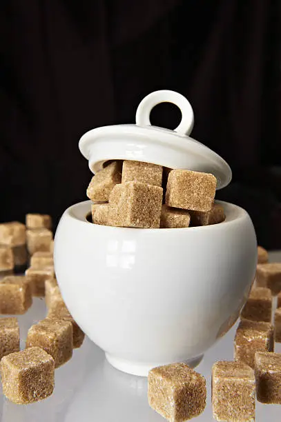 White sugarbowl with brown sugarcubes on mixed brown and white background