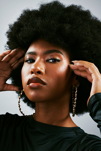 Closeup portrait of a beautiful young, stylish black woman posing against a white studio background. Unsmiling, confident, and sassy female with an afro looking empowered and showing face cosmetics